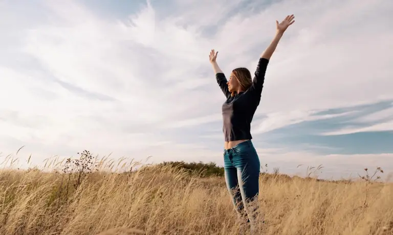 Woman standing in a field with her arms up