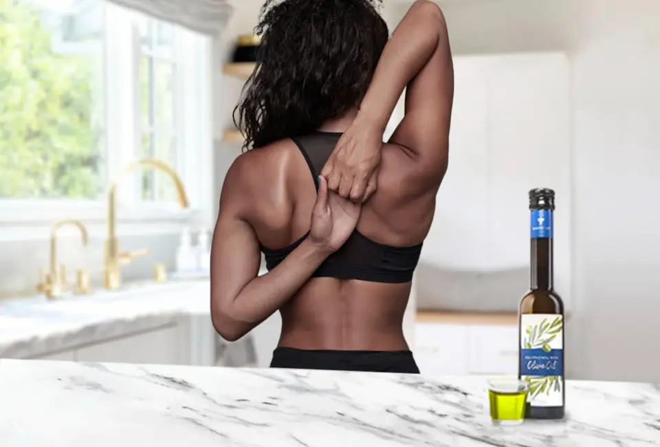 A woman in a black top stretching her upper back with a bottle of Gundry MD Olive Oil next to her