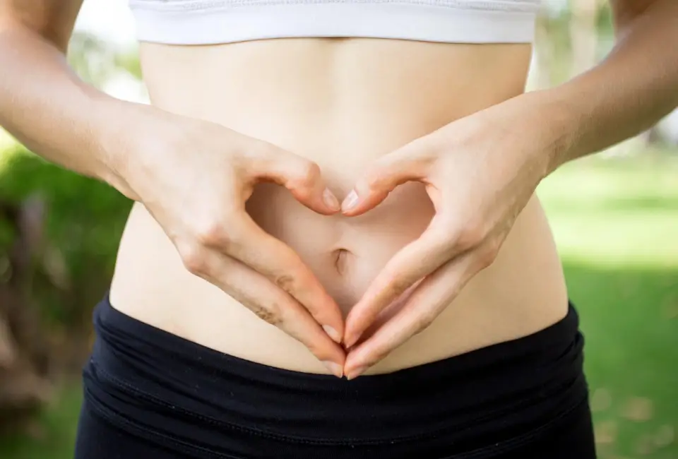 A woman making a heart shape with her hands around her belly button